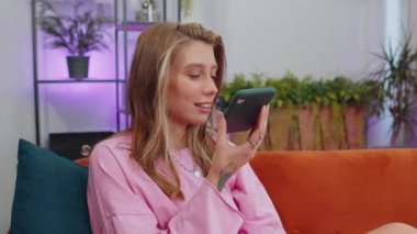 Kafkasyalı bir kızın, evdeki kanepede oturan arkadaşlarıyla telefon konuşması yaparken portresi. Mobil hoparlörlerden hoşlanan mutlu, heyecanlı genç bir kadın modern ev dairesinde kapalı mekanda konuşuyor.