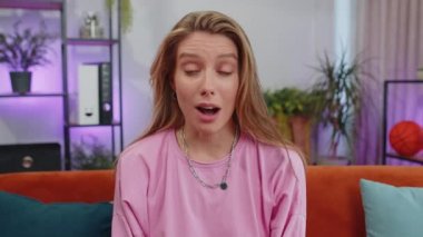 Oh my God, Wow. Lovely adult girl surprised looking at camera with big eyes, shocked by sudden victory, good win news, celebrating at home. Excited amazed young woman indoors in living room on couch