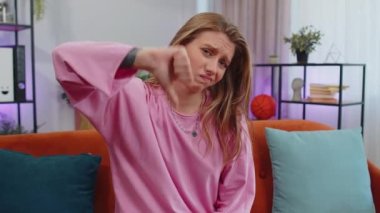 Dislike. Upset girl showing thumbs down sign gesture, expressing discontent, disapproval, dissatisfied bad work at modern home apartment indoors. Displeased young woman in living room sitting on sofa