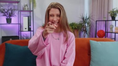 Hey you. Portrait of adult girl smiling excitedly and pointing to camera, choosing lucky winner, indicating to awesome you, inviting, approve. Young woman at modern home apartment living room on couch