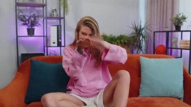 Portrait of caucasian cheerful rich girl showing wasting or throwing money around hand gesture, more tips earnings, big profit, win lottery, body language, share. Young woman at home in room on couch