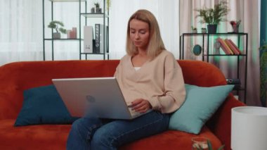 Memnuniyetle kanepede oturup dizüstü bilgisayar çığlığı atan beyaz kız zafer jesti olarak ellerini kaldırsın başarıyı kutlayalım piyangodan para kazanalım. Heyecanlı genç bayan internette iyi haberler alıyor.