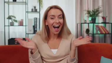 Oh my God, Wow. Lovely adult girl surprised looking at camera with big eyes, shocked by sudden victory, good win news, celebrating at home. Excited amazed young woman indoors in living room on couch