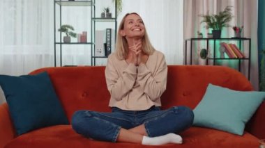 Portrait of happy calm girl in shirt smiling friendly, glad expression looking away dreaming resting, relaxation feel satisfied concept good news. Young caucasian woman sitting on sofa at home room
