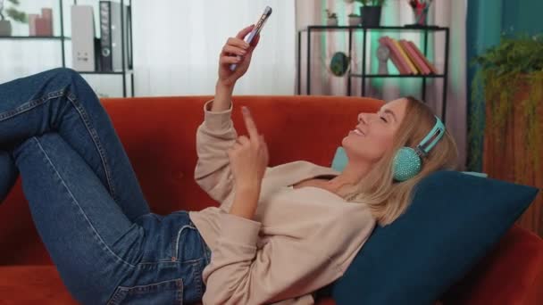 Young Woman Wireless Headphones Relaxing Lying Sofa Home Choosing Listening — Stockvideo