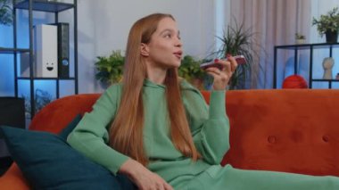 Portrait of caucasian girl making phone conversation with friends sitting call on couch at home in room. Happy excited young child kid enjoying mobile loudspeaker talking indoors at home apartment