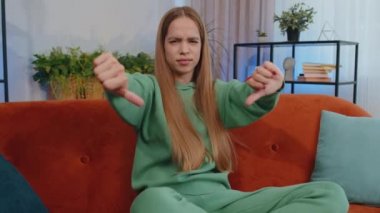 Hoşlanmamak. Sinirli kız işaret dilini gösteriyor, hoşnutsuzluğunu dile getiriyor, hoşnutsuzluğunu dile getiriyor, modern ev dairelerinde tatminsiz kötü işler yapıyor. Oturma odasındaki çocuk kanepede oturuyor.