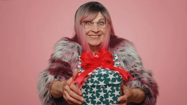 正面面带微笑的女人献上生日礼物盒 伸出双手 献上包裹着的职业奖金 庆祝派对 年长的祖母被隔离在粉红工作室的背景下 — 图库照片