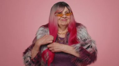 Gülümseyen, kameraya bakan, şık, şık, yaşlı bir kadın. Pembe saç stili kuaför stüdyosu olan yaşlı model büyükanne pembe arka planda izole edilmiş. Kadın doğası güzelliği