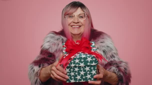 誕生日ギフトボックスを提示肯定的な笑顔スタイリッシュな女性は手を伸ばし 現在のキャリアボーナスをラップし パーティーを祝う提供しています ピンクのスタジオの背景に隔離された高齢者の祖母 — ストック動画