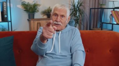 Hey sen! Kıdemli yaşlı adam heyecanlı bir şekilde gülümsüyor ve kamerayı işaret ediyor, şanslı kazananı seçiyor, muhteşem olduğunu gösteriyor, davet ediyor, onaylıyor. Yaşlı olgun büyükbaba oturma odasında kanepede oturuyor.