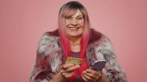 お金を転送しながら クレジットカードやスマートフォンを使用して誠実な高齢女性の顧客は オンラインショッピング 支払いを購入します 金融とインターネット ピンクの背景に隔離されたシニア祖母 — ストック写真
