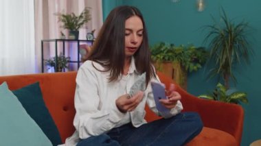 Planning family budget. Smiling caucasian girl counting money cash, use smartphone calculate domestic bills at home. Joyful young woman satisfied of income and saves money for planned vacation, gifts