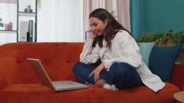 Portrait of caucasian girl sitting on couch, looking at camera, making video webcam conference call with friends or family, enjoying pleasant conversation. Young woman laughing, waving hello at home