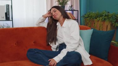 Portrait of happy calm girl in shirt smiling friendly, glad expression looking away dreaming resting, relaxation feel satisfied concept good news. Young caucasian woman sitting on sofa at home room