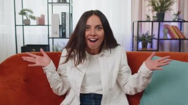 Oh my God, Wow. Lovely adult girl surprised looking at camera with big eyes, shocked by sudden victory, good win news, celebrating at home. Excited amazed young woman indoors in living room on couch