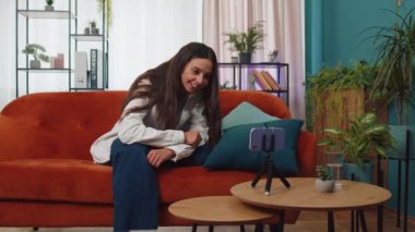 Güzel kadın blogcu cep telefonu kamerasından selfie çeken aygıt ekranına bakıyor, modern sosyal medya vlog uygulamasında sanal video görüşmesi yapıyor. Evdeki koltukta akıllı telefonlu bir kadın.