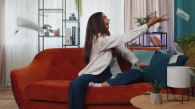 Money cash hundred euro rain falling on girl celebrating success, winning, goal achievement, good news, lottery jackpot luck at modern home office apartment indoors. Career grow. Woman sits on sofa