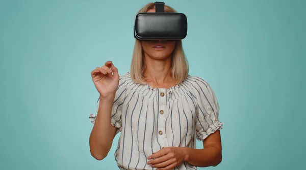 Exited stylish woman using virtual reality futuristic technology VR app headset helmet to play simulation 3D 360 video drawing game. Young adult girl on blue studio background. People sincere emotions