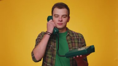 Hey sen, beni ara. Yeşil tişörtlü neşeli sekreter 80 'lerin telli vintage telefonundan konuşuyor. Beni geri ara diyor. Sarı stüdyo arka planında izole edilmiş genç bir adam.