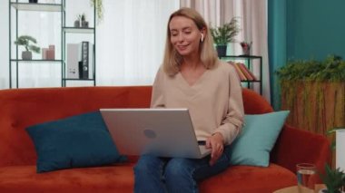 Portrait of caucasian girl sitting on couch, looking at camera, making video webcam conference call with friends or family, enjoying pleasant conversation. Young woman laughing, waving hello at home