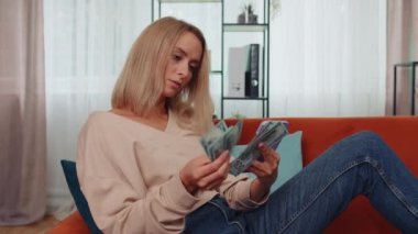 Planning family budget. Smiling caucasian girl counting money cash, use smartphone calculate domestic bills at home. Joyful young woman satisfied of income and saves money for planned vacation, gifts