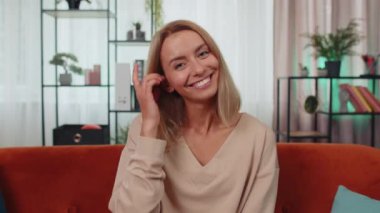 Close-up portrait of happy smiling caucasian girl in shirt, looking at camera, celebrate good news. Young woman indoor isolated at home in living room sitting on orange couch. Female nature beauty
