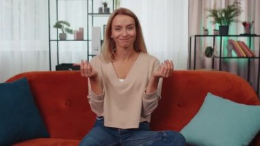 Portrait of caucasian cheerful rich girl showing wasting or throwing money around hand gesture, more tips earnings, big profit, win lottery, body language, share. Young woman at home in room on couch