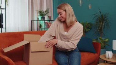 Portrait of happy girl unpacking delivery parcel sitting at home. Smiling satisfied young woman shopper, online shop customer opening cardboard box receiving purchase gift by fast postal shipping