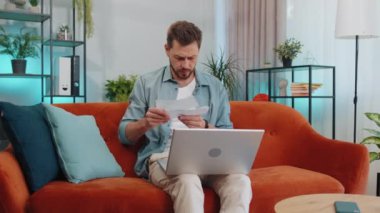 Evde stresli bir adam, ödenmemiş banka borçlarına bakıyor evrak işleriyle uğraşıyor, bütçe planlıyor, ev kredisi ödemelerini hesaplıyor. Memnun olmayan genç adam turuncu kanepeye kağıt para atıyor.