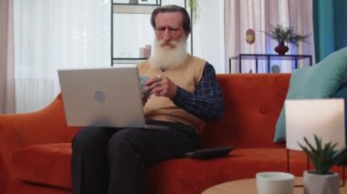 Planlama bütçesi. Zengin mutlu büyükbaba para sayıyor dizüstü bilgisayar kullanıyor evde faturaları hesaplıyor. Kazancından memnun olan neşeli yaşlı adam, planlı tatil hediyeleri için para biriktiriyor.