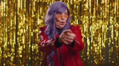 Tarz sahibi, mutlu bir kadın etrafta parmak tabancasıyla işaret ediyor, kendinden emin görünüyor, seçim yapıyor, tabancayla hedefi vuruyor. Parlak parti geçmişi olan yaşlı bir büyükanne.