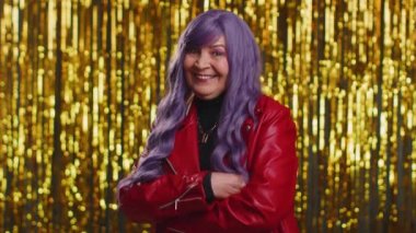 Kırmızı ceketli, gülümseyen, kameraya bakan neşeli, şık, şık, yaşlı bir kadın. Parlak disko partisinin arka planında, mor saç stili kabarık, son sınıf moda model yaşlı bir büyükanne.