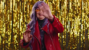 Buraya gel, bize katıl. Hoş geldiniz. Olgun stil sahibi bir kadın elleriyle davetkar bir jest yapıyor, katılmak istiyor, gelmek için işaret ediyor, merhaba ya da elveda diyor. Parlak disko partisi geçmişi olan büyük anne.