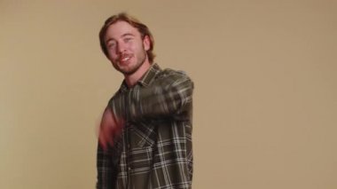 Come here, join us. Welcome. Handsome bearded man showing inviting gesture with hands, ask to join, beckoning to coming, gesturing hello or goodbye. Young guy boy isolated on beige studio background