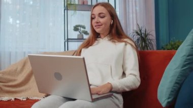 Portrait of caucasian girl sitting on couch, looking at camera, making video webcam conference call with friends or family, enjoying pleasant conversation. Young woman laughing, waving hello at home