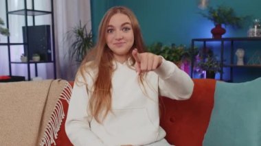 Hey you. Portrait of adult girl smiling excitedly and pointing to camera, choosing lucky winner, indicating to awesome you, inviting, approve. Young woman at modern home apartment living room on couch