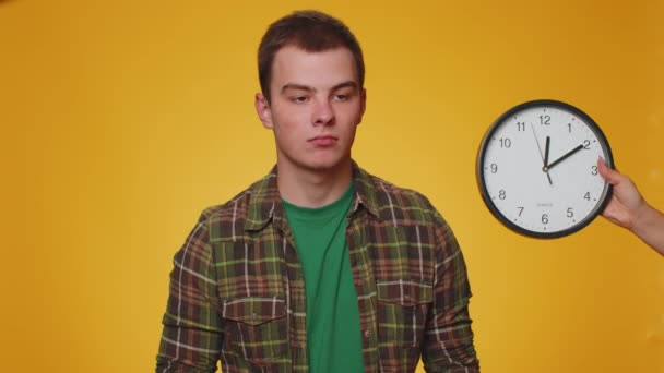 困惑的年轻人与焦虑的检查时间在时钟上 运行迟到 黄色工作室背景的最后期限 认真的男孩看着时间和分钟 担心准时 — 图库视频影像