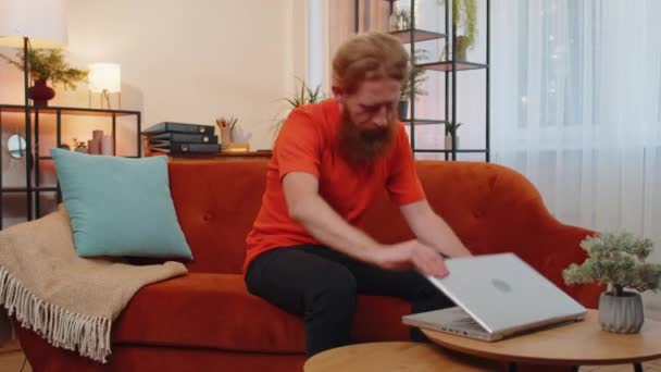 거실에서 오렌지 소파에 노트북을 젊은이는 노트북으로 일하고 메시지를 보내고 온라인 — 비디오