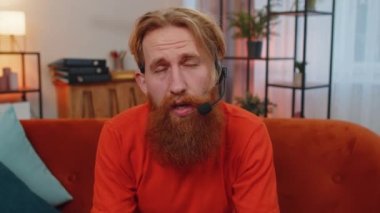Kulaklık takan sakallı adam POV 'u, serbest çalışan, çağrı merkezi ya da destek operatörü yardım hattı, müşteri ya da iş arkadaşı ile iletişim desteği ile evde tek başına el sallayarak merhaba diyor.
