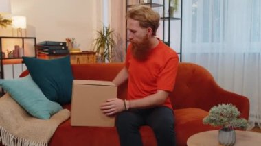 Happy surprised winner adult man unpacking delivery parcel at home. Smiling satisfied young guy shopper, online shop customer opening cardboard box receiving purchase gift ball by fast postal shipping
