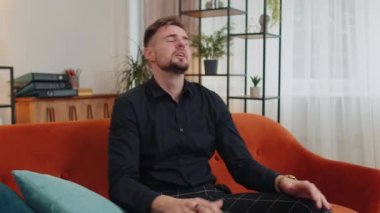 Depresyondaki genç sakallı adam stres gerginliğinden bağırıyor korku, umutsuzluk, şaşkınlık şaşkınlık jestler, öfke. Evde turuncu koltukta oturan öfkeli iş adamı.