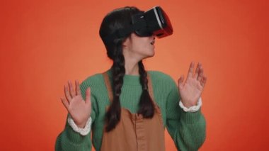 Çevrimiçi oyun uygulaması oynamak için kulaklık kullanan genç bir kadın. Sanal gerçeklik 3D 360 video içeriği izliyor. VR gözlüklü Latin kız stüdyo turuncu arka planda izole edilmiş. Gelecekçi teknoloji