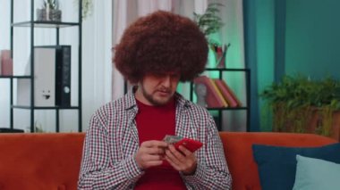 Aile bütçesi planlamak. Tüylü saç stili olan nakit para sayan bir adam akıllı telefon kullanıyor ve evdeki faturaları hesaplıyor. Gelirden memnun olan neşeli genç adam planlı tatil ve hediyeler için para biriktiriyor.