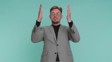 Aman Tanrım, vay canına. Heyecanlı kazanan iş adamı büyük gözlerle kameraya bakarken şaşkınlıkla el kaldırıyor, ani zaferden şok oluyor. Mavi stüdyo arka planında soyutlanmış samimi, yetişkin bir çocuk.