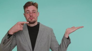 Yakışıklı bir iş adamı gösterip boş bir yeri işaret ediyor. Ticari metinler için reklam alanı, ürün tanıtımı için kopya alanı. Genç bir yetişkin. Mavi duvar arka planında kapalı stüdyo çekimi