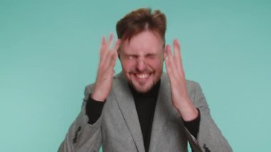 Ceket giymiş bir iş adamı stres gerginliğinden bağırıyor. Korku, umutsuzluk, şaşkınlık, şaşkınlık, öfke, jestler. Genç yetişkin erkek çocuk mavi stüdyo arka planında tek başına.