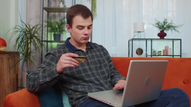 青少年男子在汇款 网上购物 在家里订购食品时使用信用卡和手提电脑的肖像 小伙子坐在家里客厅的沙发上 — 图库视频影像