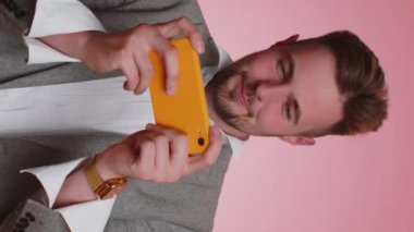 Endişeli sakallı iş adamı heyecanlı bir şekilde akıllı telefondan yarış ya da video oyunu oynuyor. Genç adam cep telefonuyla piyango ikramiyesini kutluyor, iyi haber, gol. Dikey görünüm