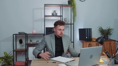 Çatışma, tartışma, pazarlık. Resmi takım elbiseli kızgın işadamı ofis masasında web kameralı bilgisayar görüşmesi yapıyor. Konsantre olmuş kızgın erkek serbest çalışan adam içeride konuşuyor.